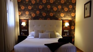 Una habitación de hotel con una cama grande, dos mesitas de noche con lámparas, un papel tapiz floral y un certificado enmarcado en la pared.