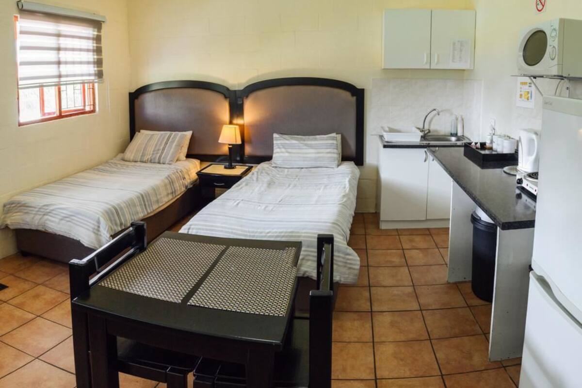 A room with two beds, a small table, a desk, and a kitchenette.