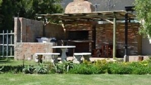 A stone-built outdoor kitchen with a chimney, surrounded by a stone wall and a wooden pergola. - Kingfisher Hollow Exclusive Guest House (Cape Town)