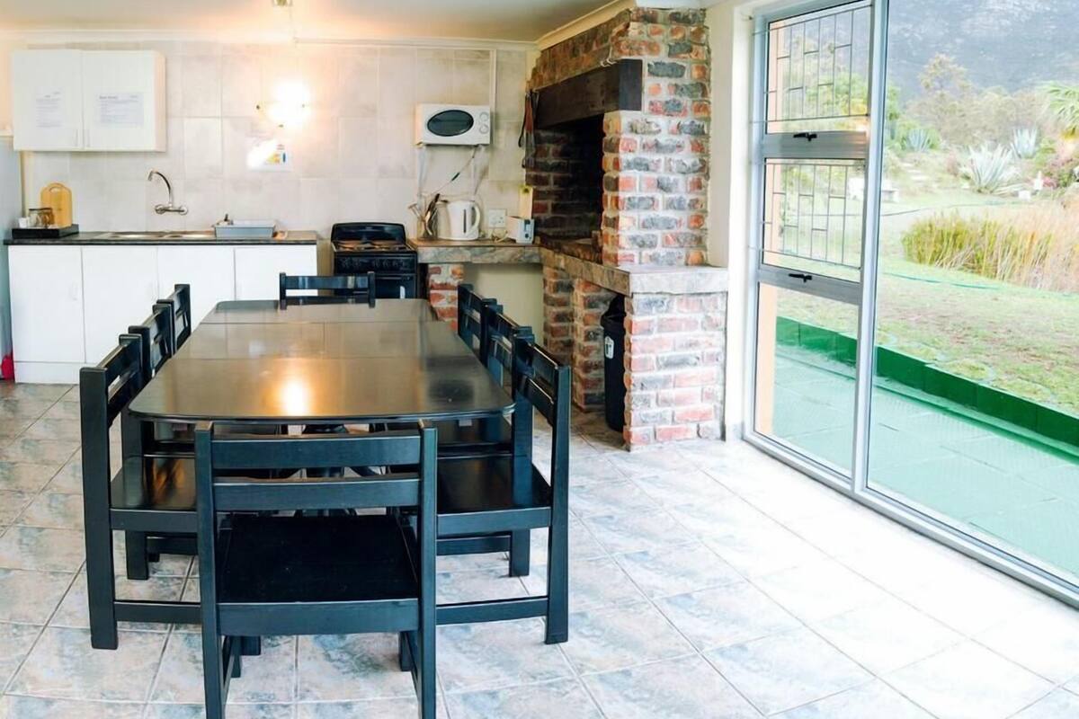 A kitchen with a brick oven, a dining table with chairs, a large window, and a view of the outdoors.