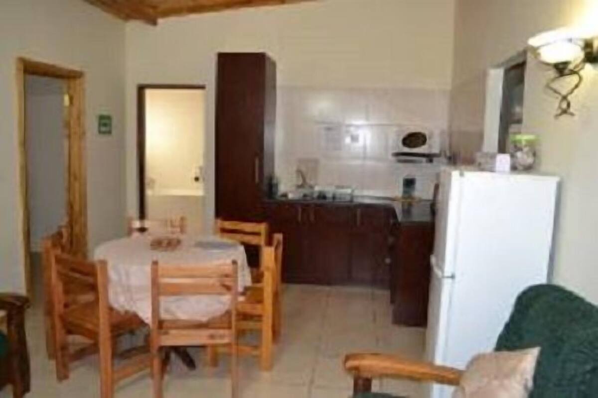 A compact kitchen with wooden cabinets, a dining table with chairs, and a refrigerator.