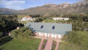 A large house with a green roof, surrounded by a well-maintained lawn and trees, with mountains in the background. - Kingfisher Hollow Exclusive Guest House (Cape Town)