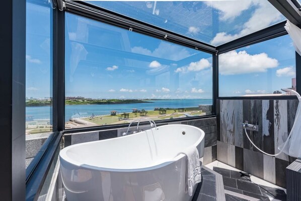 Ein modernes Badezimmer mit freistehender Badewanne, großen Fenstern mit Blick auf ein Gewässer und das Umland.