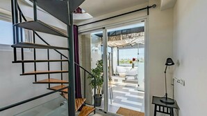 Un interior modern amb una escala de vidre, una vista d'un paisatge urbà a través d'una porta de vidre, una banyera i una planta en test.