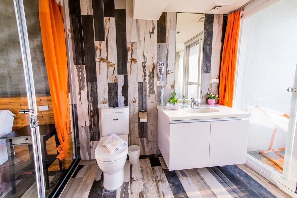 A modern bathroom with a marble wall, white fixtures, and orange curtains.