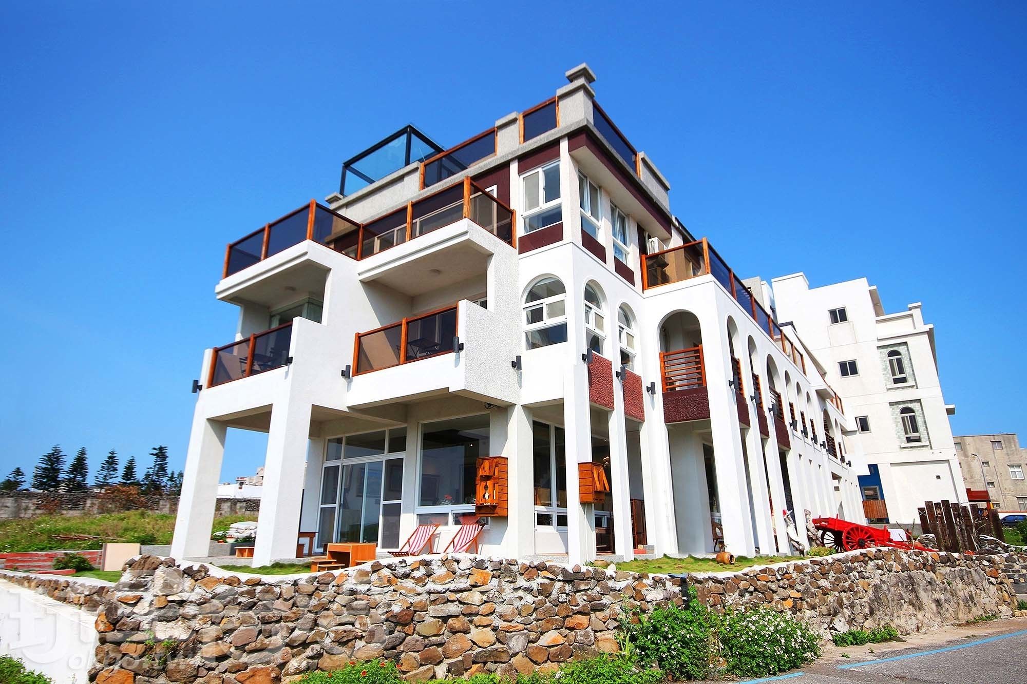 Un edificio de varios pisos con balcones, ventanas grandes y un muro de piedra frontal.