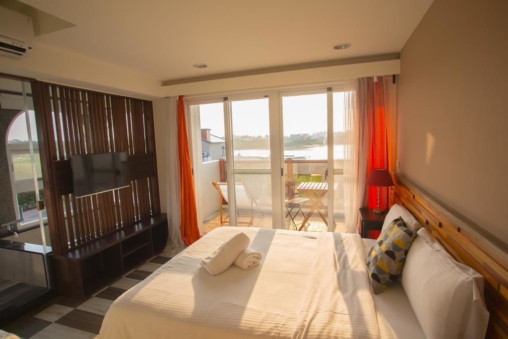 Une chambre d’hôtel avec un grand lit, une télévision, un balcon avec une table et des chaises, et une vue sur l’extérieur.