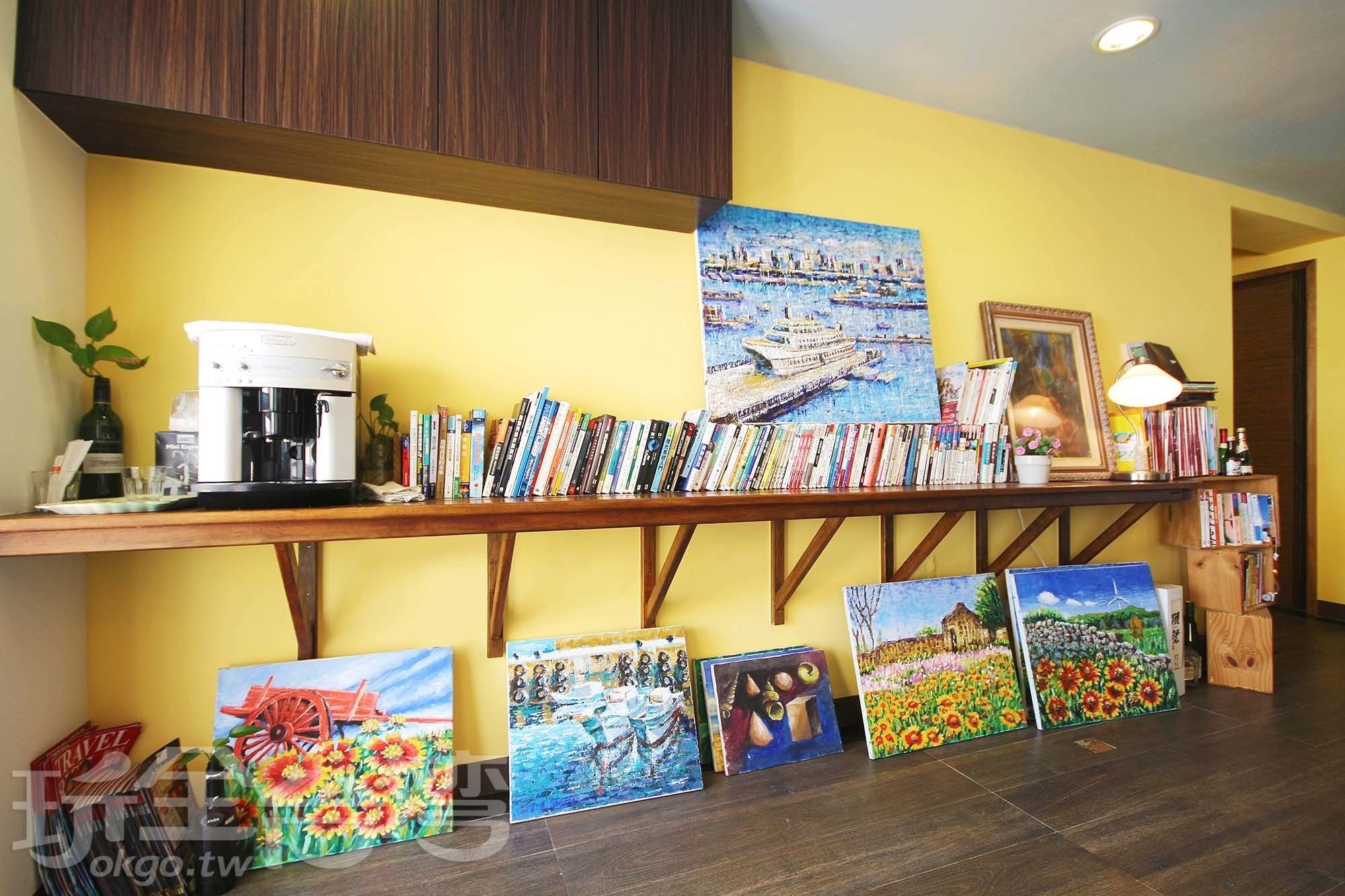 Habitació amb taula de cafè de fusta que mostra llibres i quadres, una màquina de cafè, una làmpada i un quadre encimbellat a la paret.