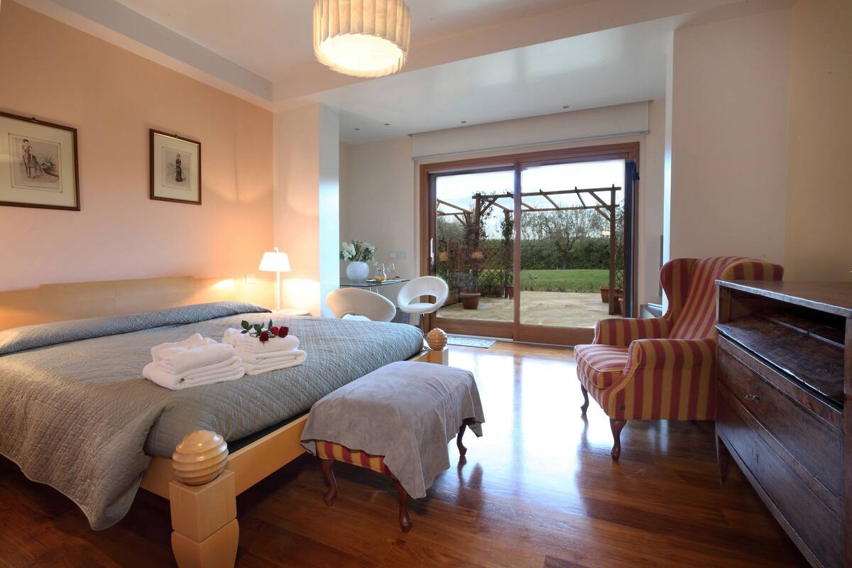 Une chambre avec un grand lit, une chaise, une commode et une vue sur l’extérieur grâce à une porte vitrée.