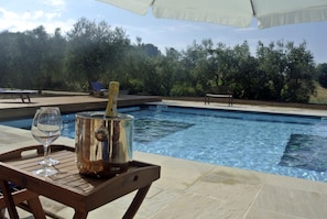 A poolside area with a table holding a champagne bottle and glass, surrounded by trees and a clear sky. - Agriturismo La Limonaia (Mondavio)