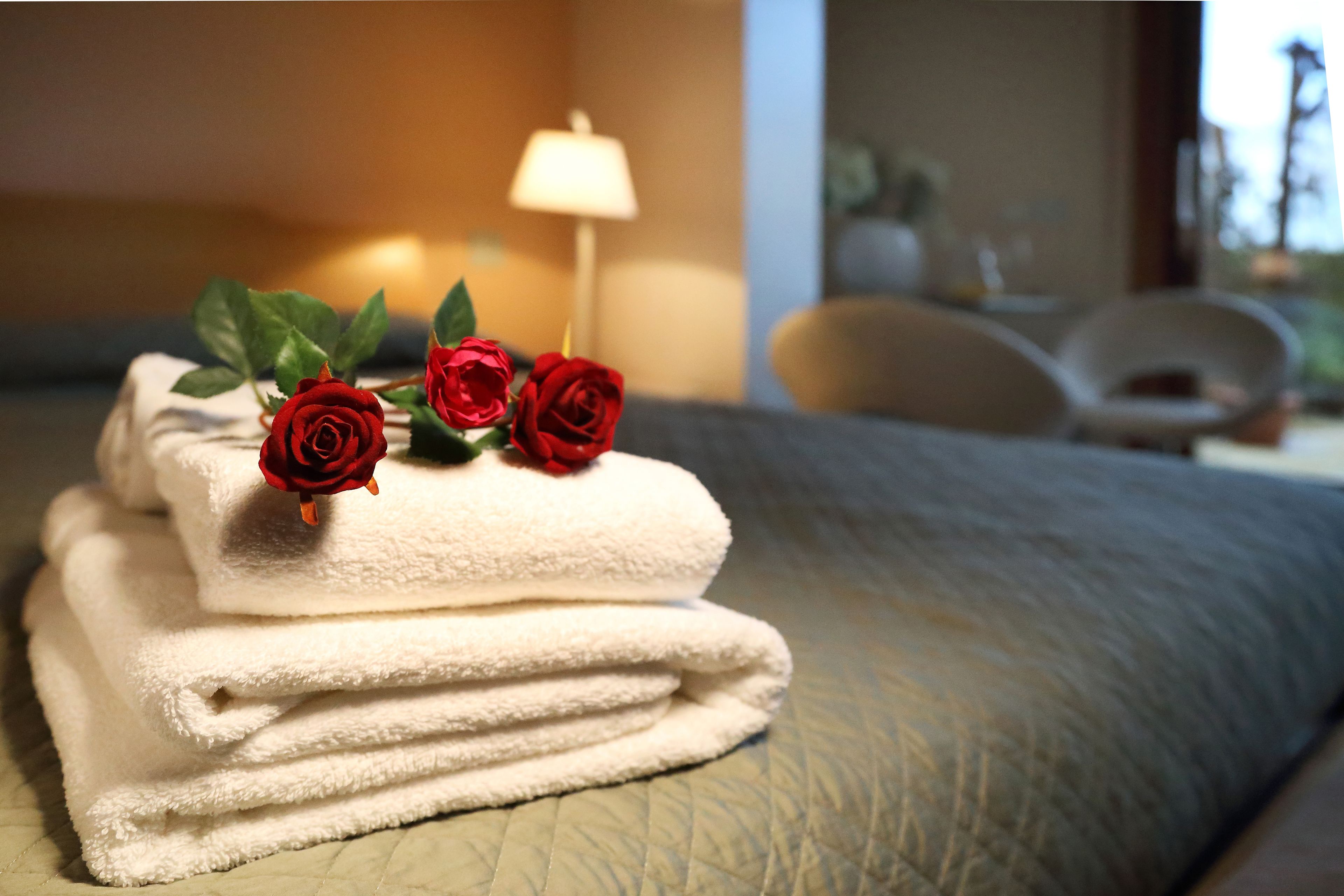 Un montón ordenado de toallas blancas con rosas rojas encima, sobre una cama con cubrecama acolchado.