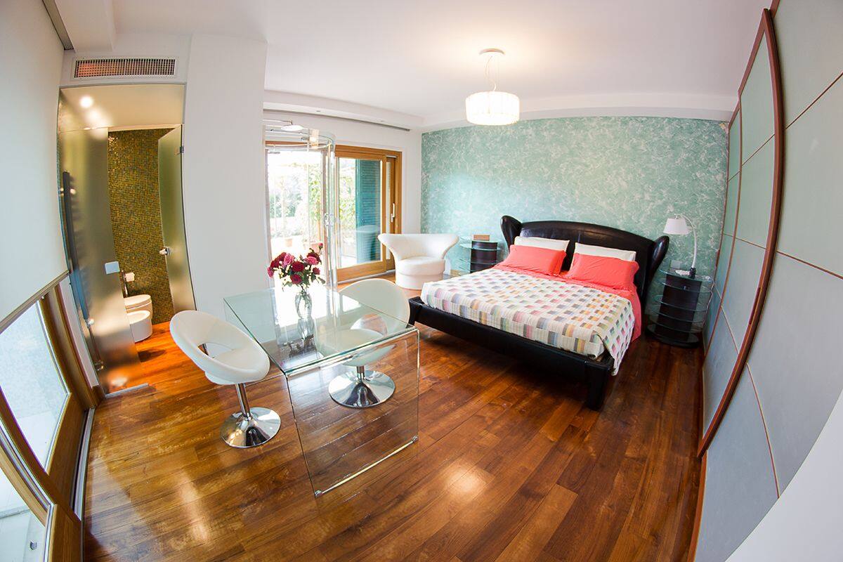 Une chambre moderne avec une table en verre, un lit recouvert d’une couverture à carreaux et une vue sur l’extérieur.