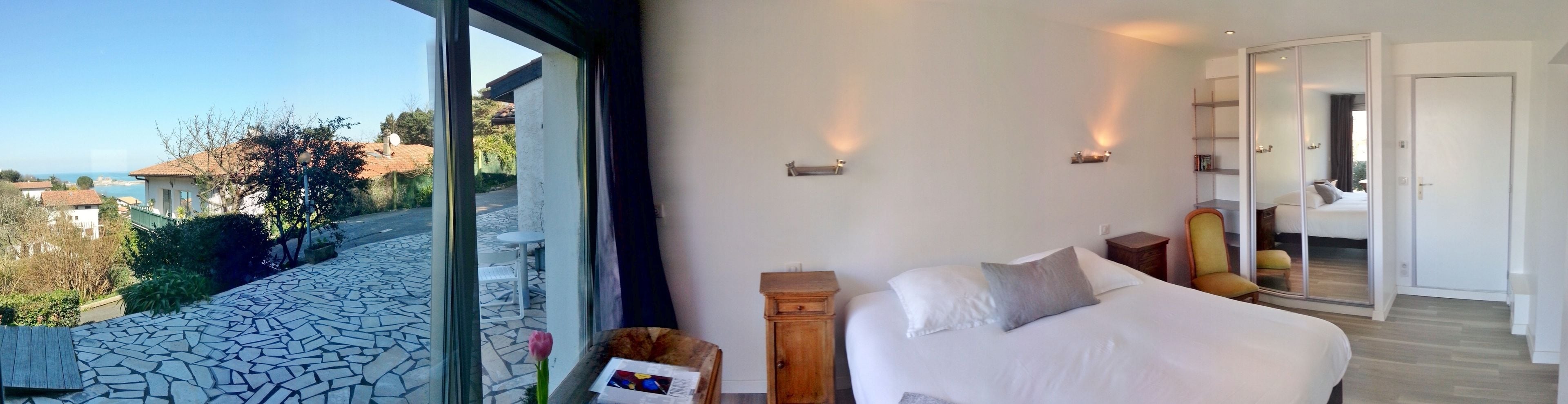 Un dormitorio con un ventanal grande, una cama, una mesita de noche y un armario de madera.