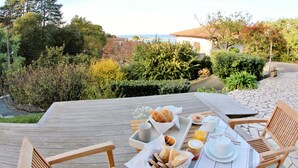 Una terraza de madera con una mesa dispuesta para el desayuno, incluyendo pan, bollería y bebidas.