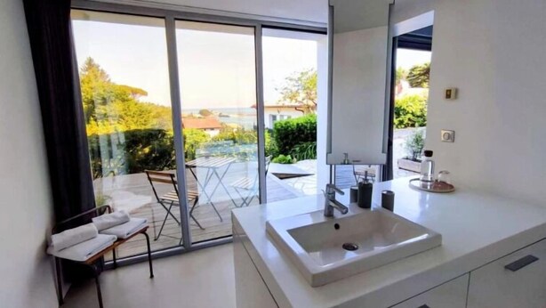 Un baño moderno con un ventanal amplio, un lavabo blanco y una silla con toallas.
