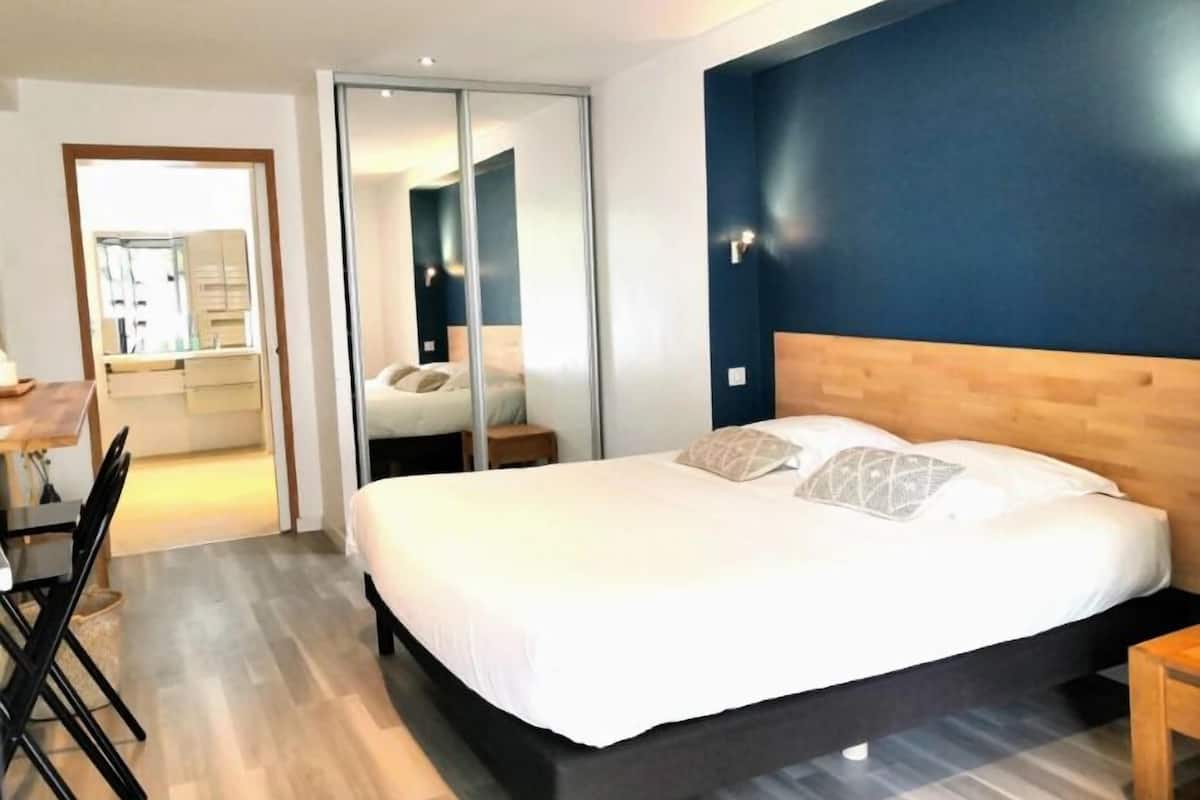A bedroom with a large bed, a wooden headboard, a bedside table, and a mirror.