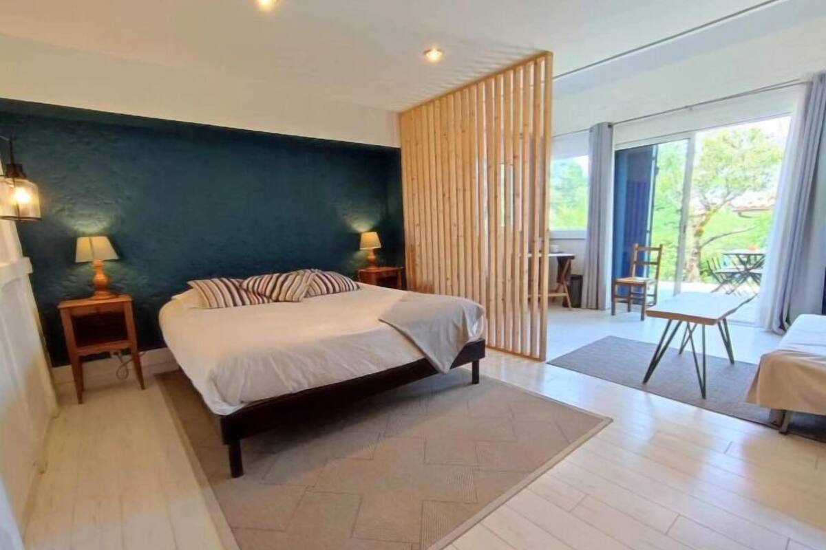 A modern bedroom with a large bed, two bedside tables with lamps, a dark blue accent wall, and a view of the outdoors.