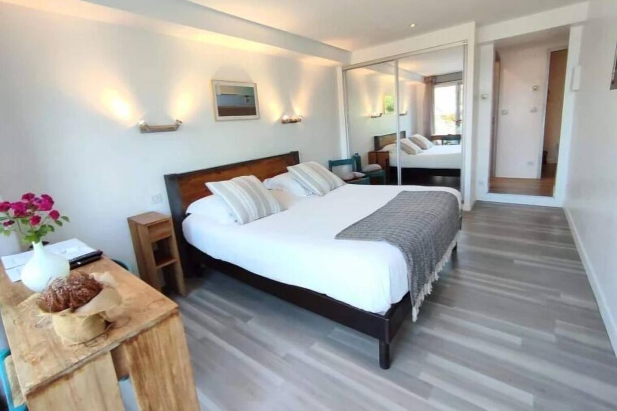 A modern bedroom with a large bed, bedside tables, a mirror, and a wooden nightstand.