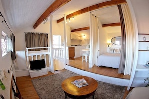 Una habitación pequeña y luminosa, con techo de madera, televisión, una mesita y una cama.