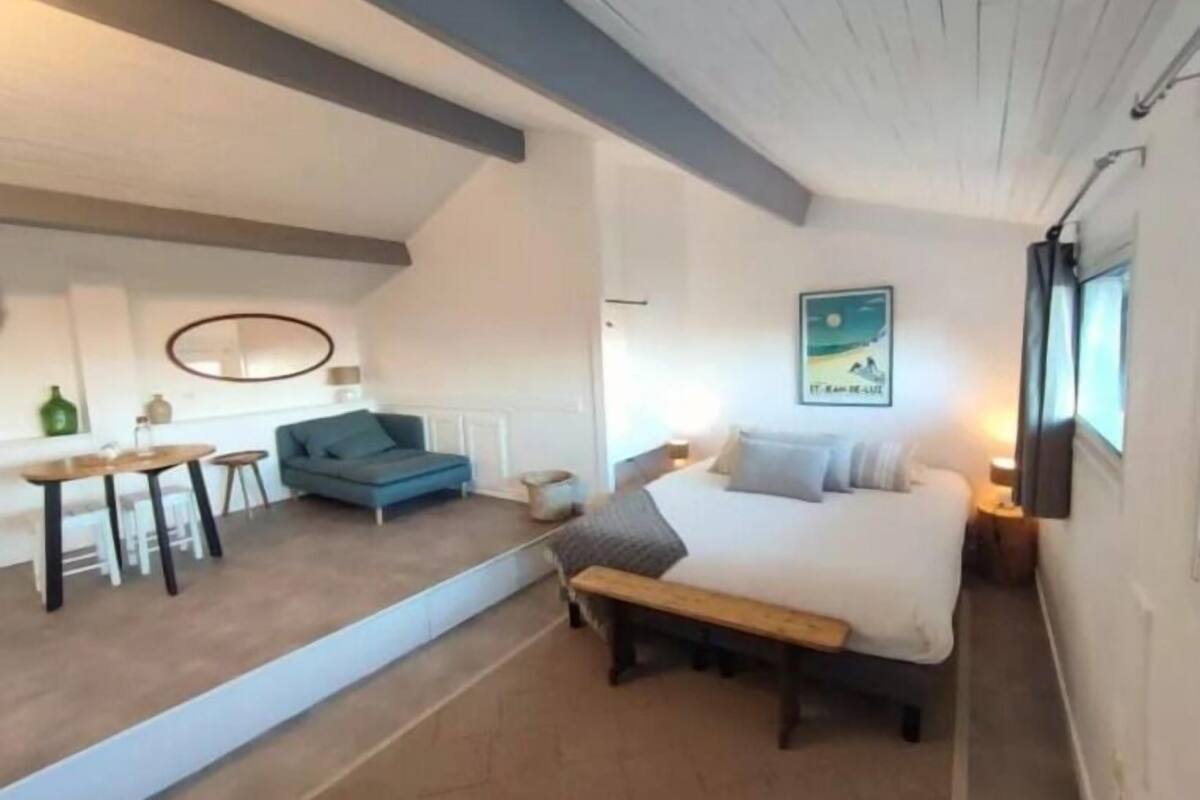 A bedroom with a bed, a bench, a blue sofa, a small table, and a wall-mounted lamp.