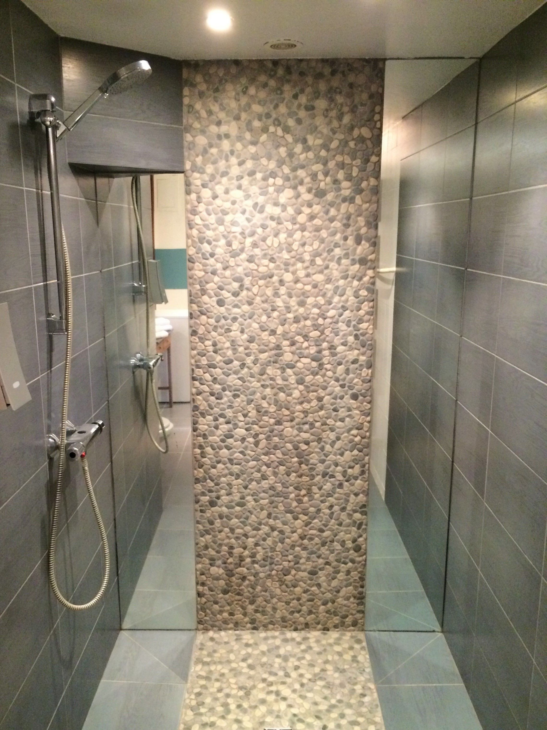 A narrow shower area with a pebble wall, tiled floor, and a glass-enclosed shower stall.