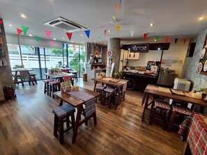 A restaurant with wooden tables and chairs, a bar area, and a view through large windows. - Boutique Poo-Yai Lee (Bangkok)