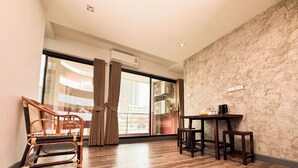 Una habitación con piso de madera, una mesa de comedor con sillas, una silla de mimbre, una puerta corrediza de vidrio con cortinas y una pared con textura de piedra.
