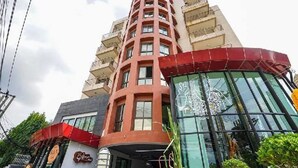 Un hotel de varios pisos con una fachada llamativa en rojo y beige, amplios ventanales de vidrio y un logotipo visible en la construcción.