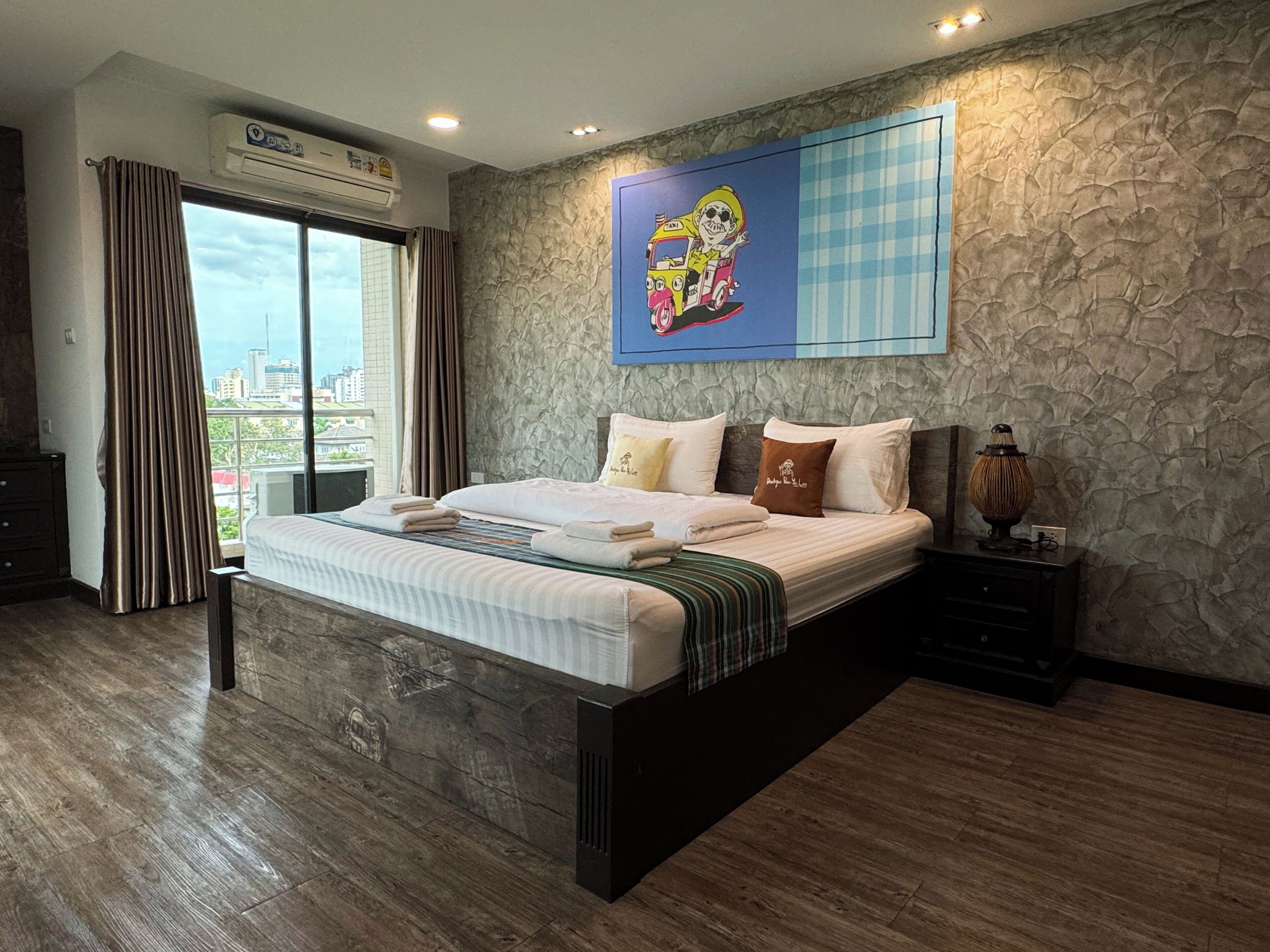 A bedroom with a large bed, a city view, a stone wall, and a painting.