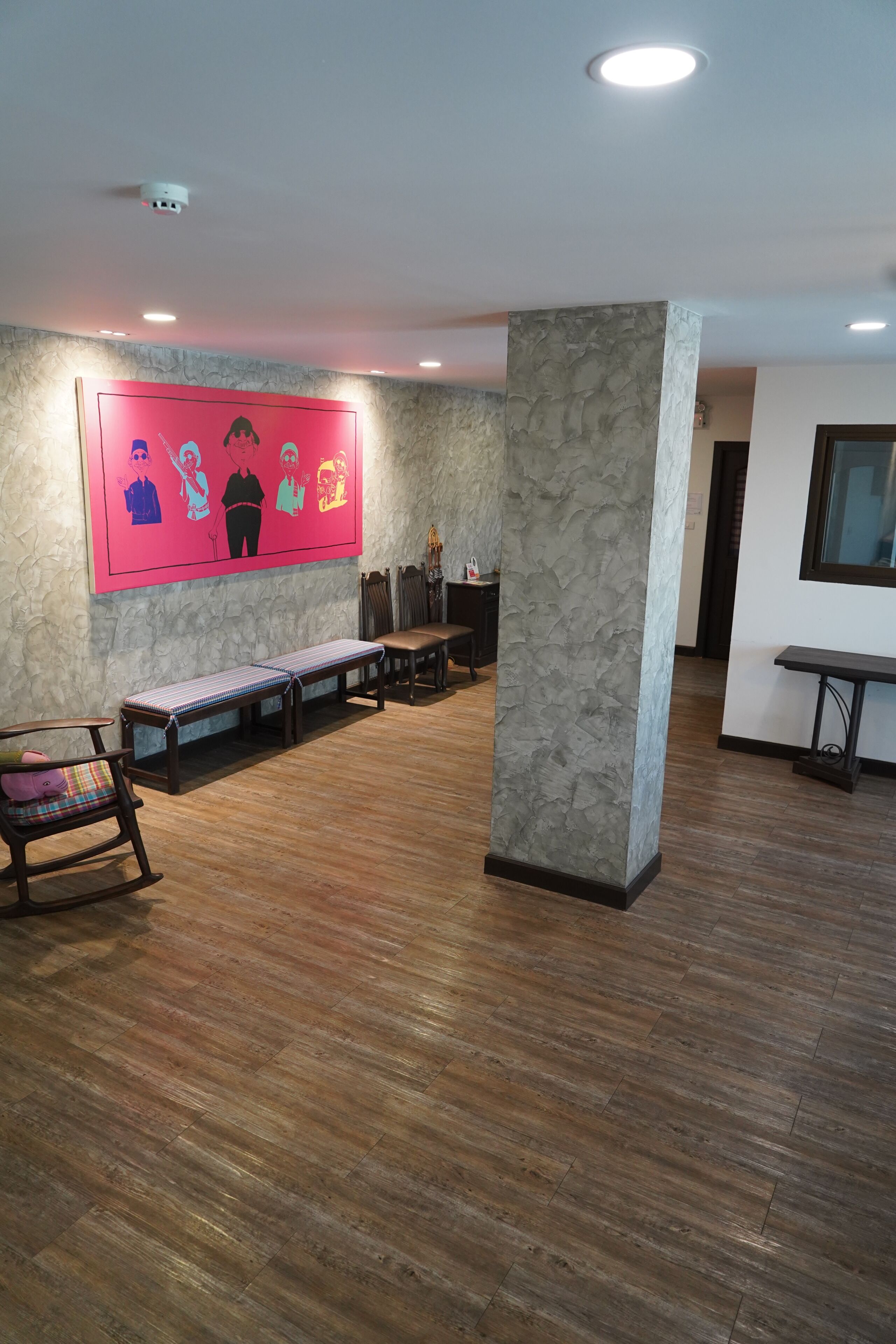 A spacious lobby with a stone pillar, wooden flooring, a bench, and a colorful mural on the wall.