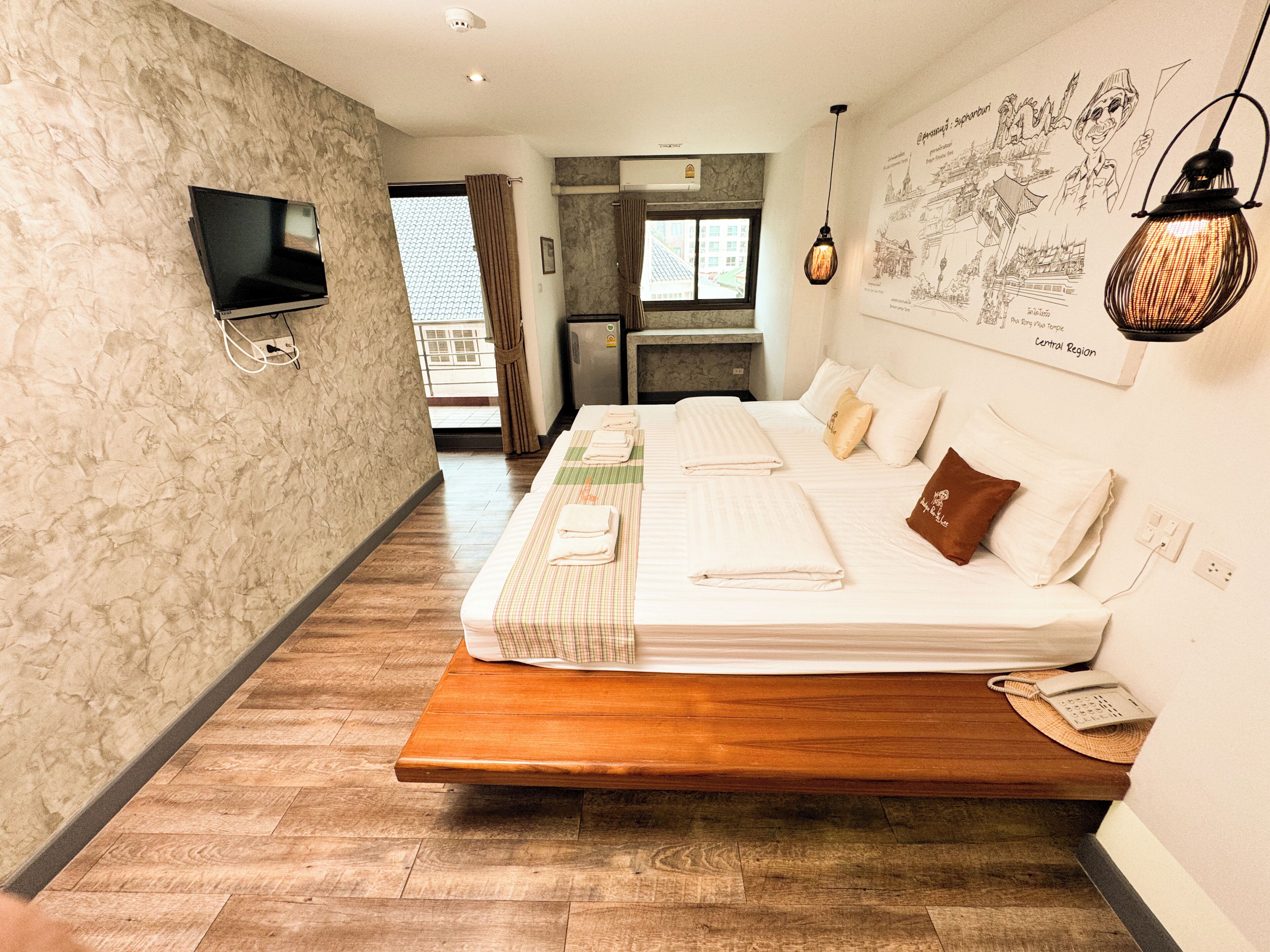 A hotel room with a bed, a TV, a desk, and a wall with drawings.