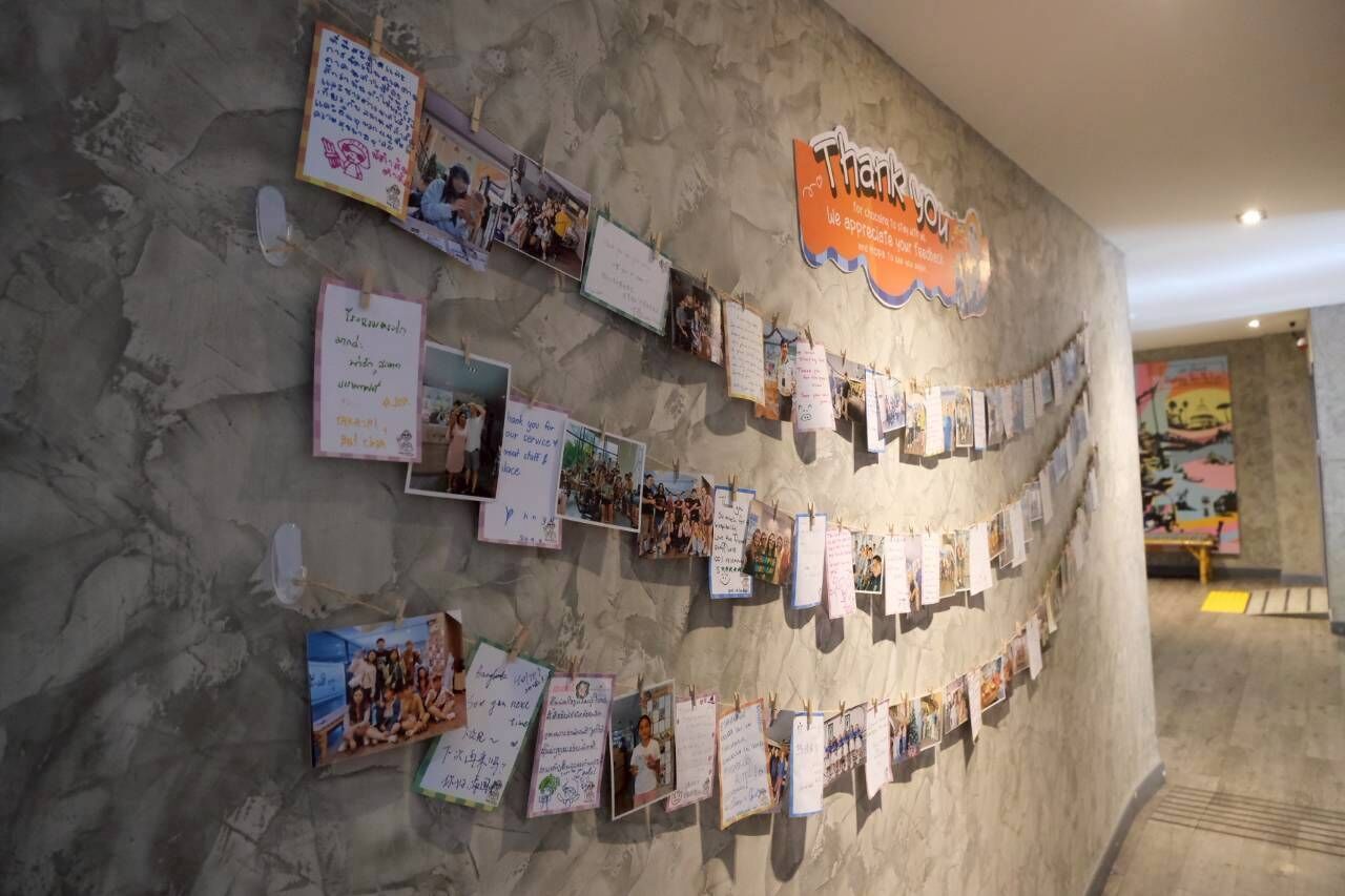 A wall with various notes and photos pinned to it, a 'Thank You' sign, and a partial view of a colorful mural in the background.