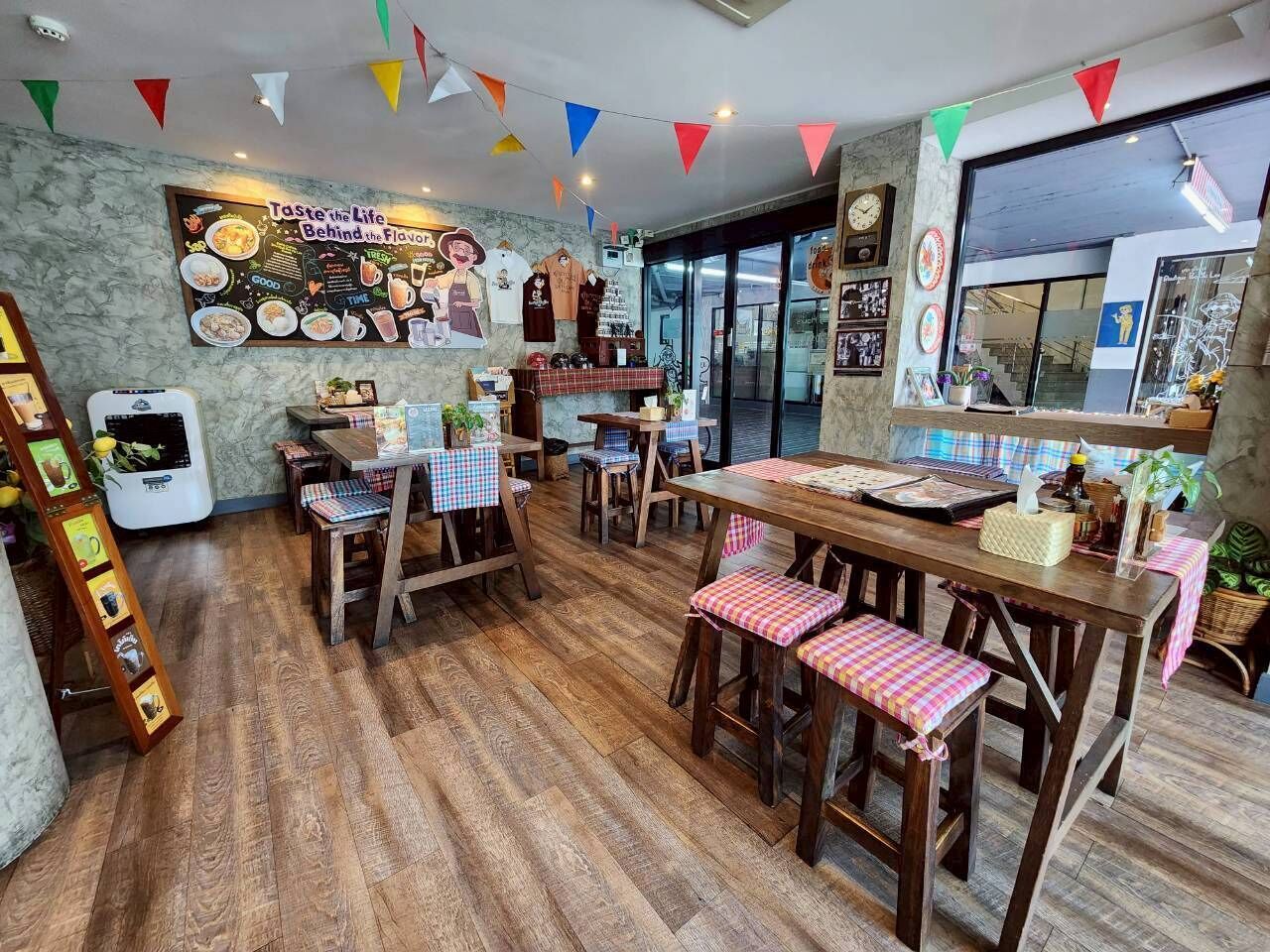 Interior de restaurante con mobiliario de madera, menú en pizarra y banderas triangulares coloridas.