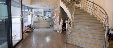 Un hall de hotel con una escalera, una mesa de recepción y un escaparate de vidrio.