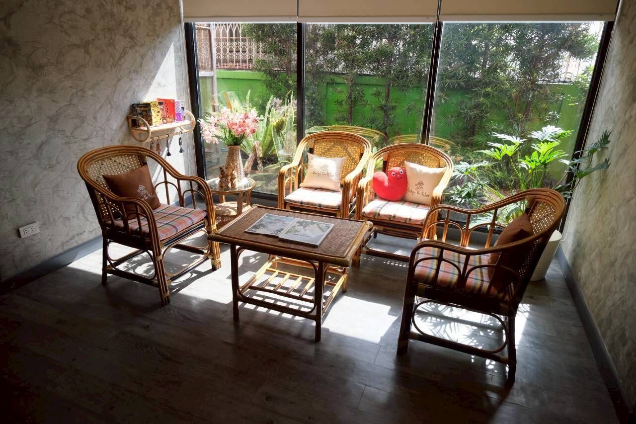 A room with wicker furniture, a table with papers, and a view of greenery outside.