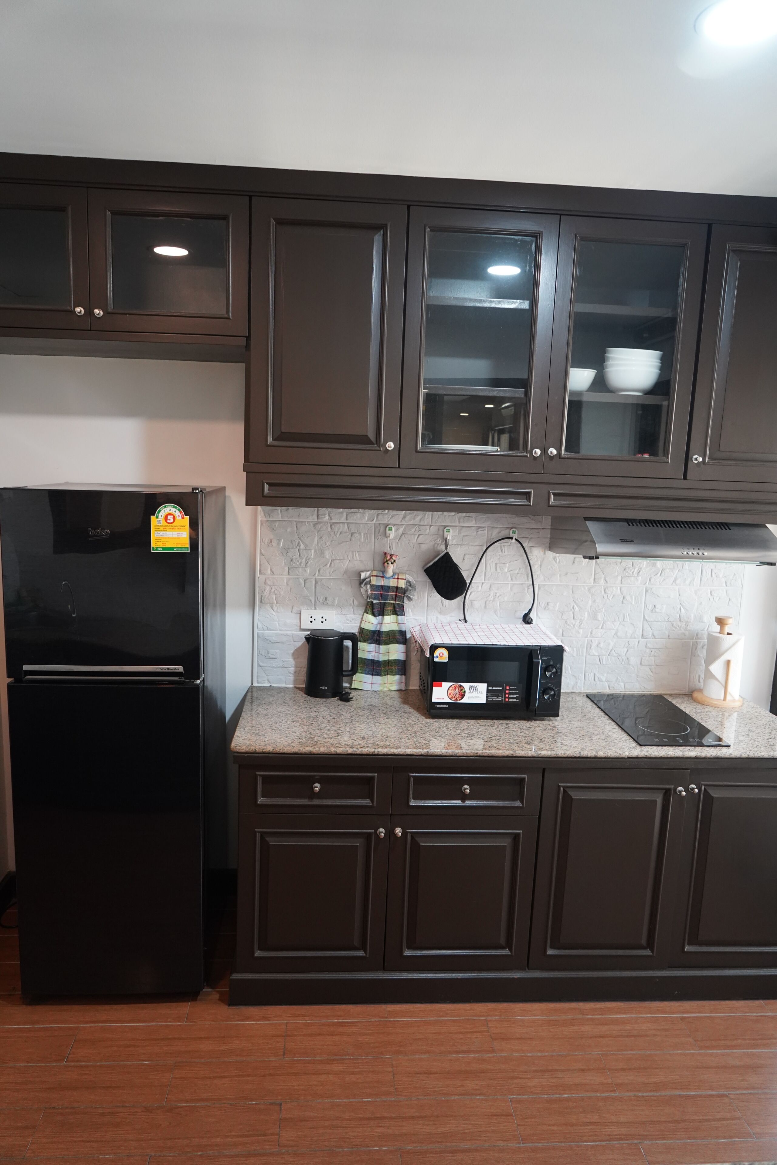 A kitchen with dark brown cabinets, a black refrigerator, a microwave, and a gas stove.