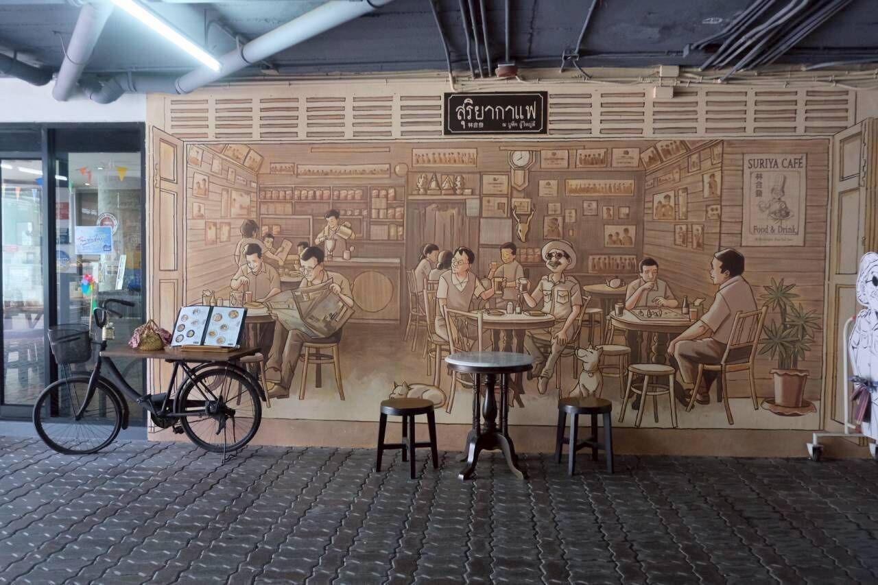 Un mural que representa una terrassa de cafè amb taules i cadires, una bicicleta i un cartell al damunt.