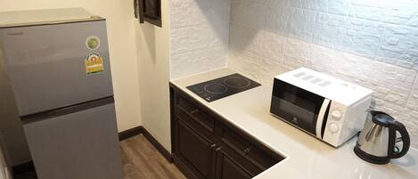 Una cocina compacta equipada con refrigerador, microondas, cocina por inducción y hervidor.