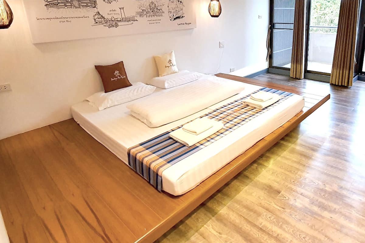 Una habitación de hotel moderna con una cama grande, suelo de madera, vistas por la ventana y una pared decorada con obras de arte.