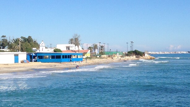 Un paysage côtier avec un bâtiment bleu, une plage de sable et l’océan.