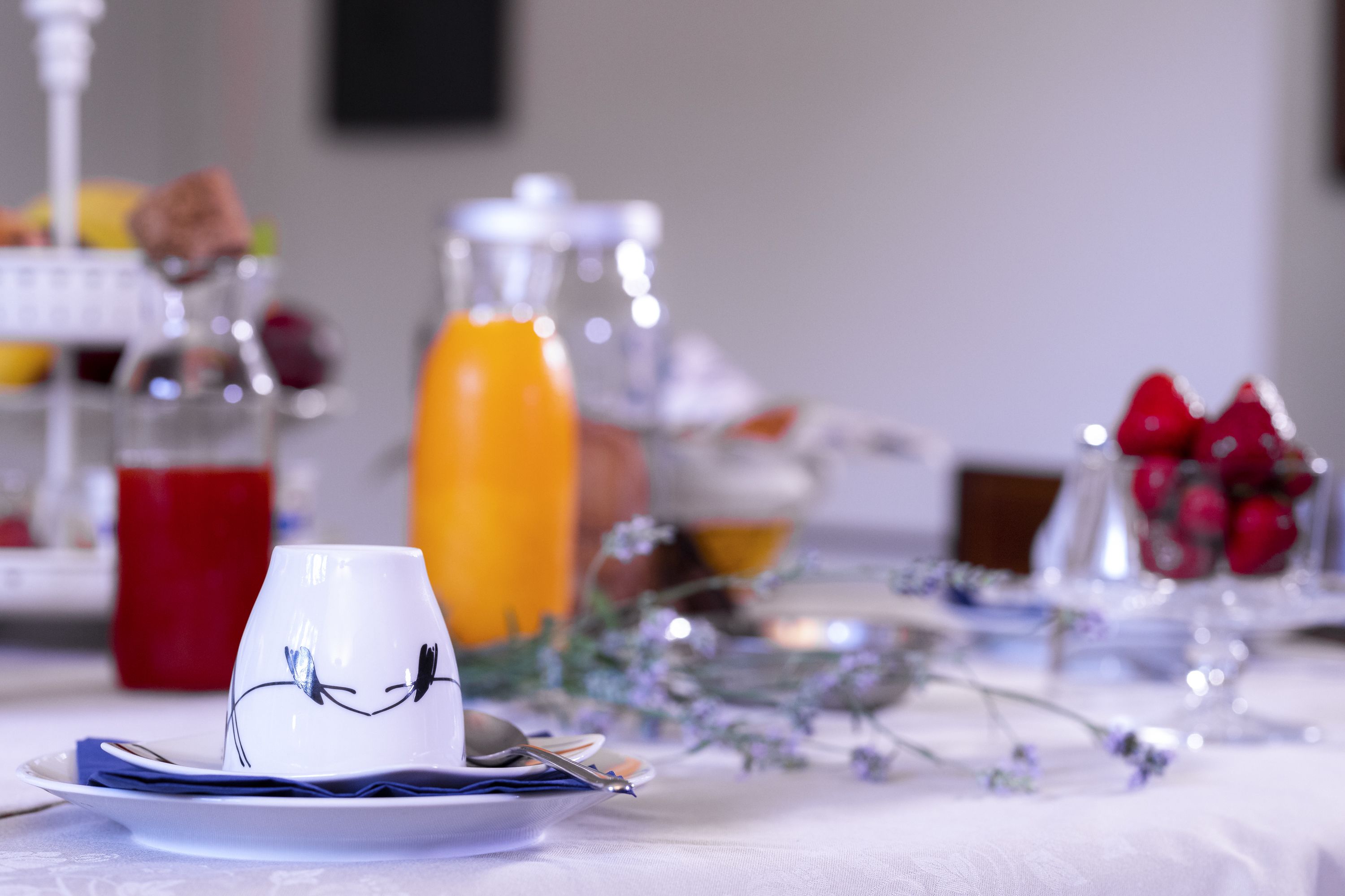 Desayuno con una taza blanca, un platito y una cuchara, un vaso de jugo de naranja y un bol de frutas con bayas rojas.