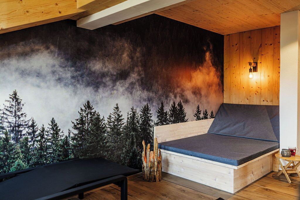 A cozy room with a bed, a bench, and a wall mural of a forest.