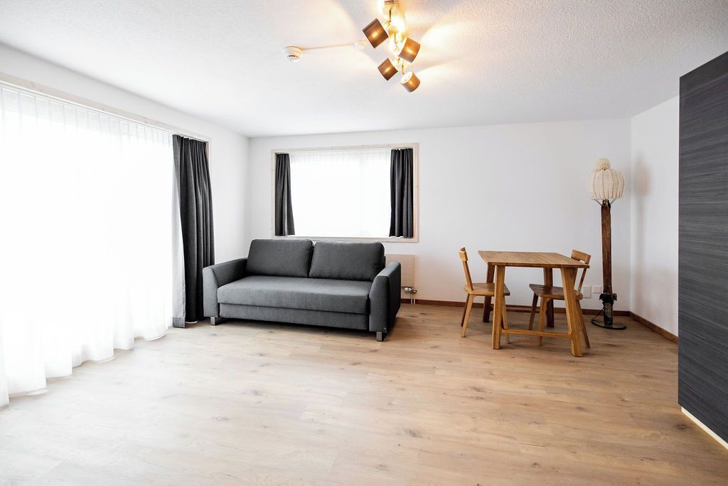 Een moderne woonkamer met een grijze bank, een houten eettafel en een vloerlamp.
