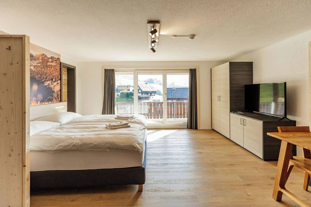 Ein Hotelzimmer mit einem großen Bett, einem Fernseher, einem Holztisch und einem Balkon mit Bergblick.