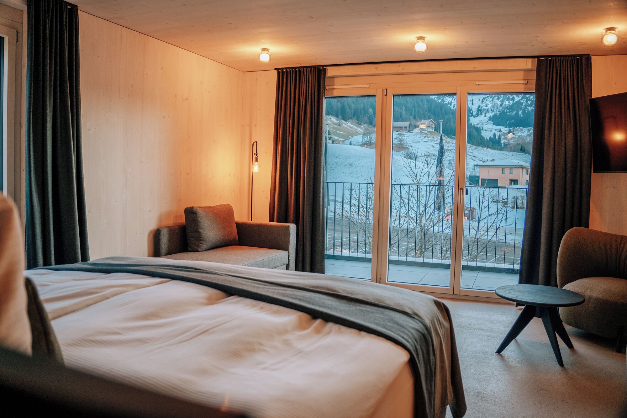 Een hotelkamer met een groot bed, een bank, een tafeltje en een balkon met uitzicht op een besneeuwd landschap.