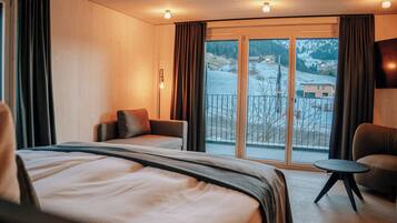 Een hotelkamer met een groot bed, een bank, een tafeltje en een balkon met uitzicht op een besneeuwd landschap.