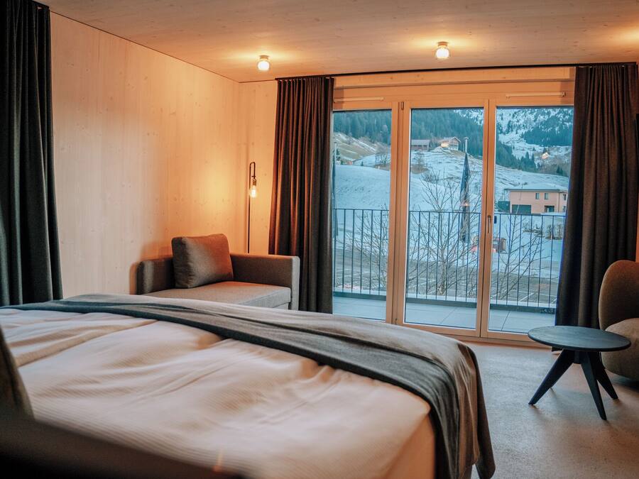 Een hotelkamer met een groot bed, een bank, een tafeltje en een balkon met uitzicht op een besneeuwd landschap.