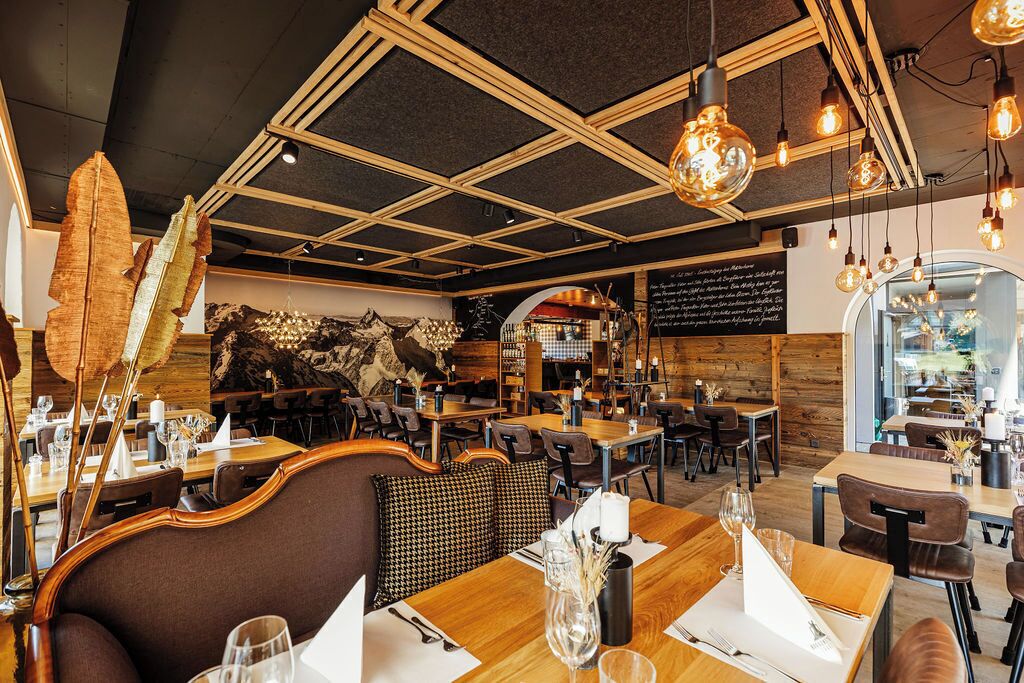 A restaurant interior with wooden tables, hanging light fixtures, and a mural on the wall.