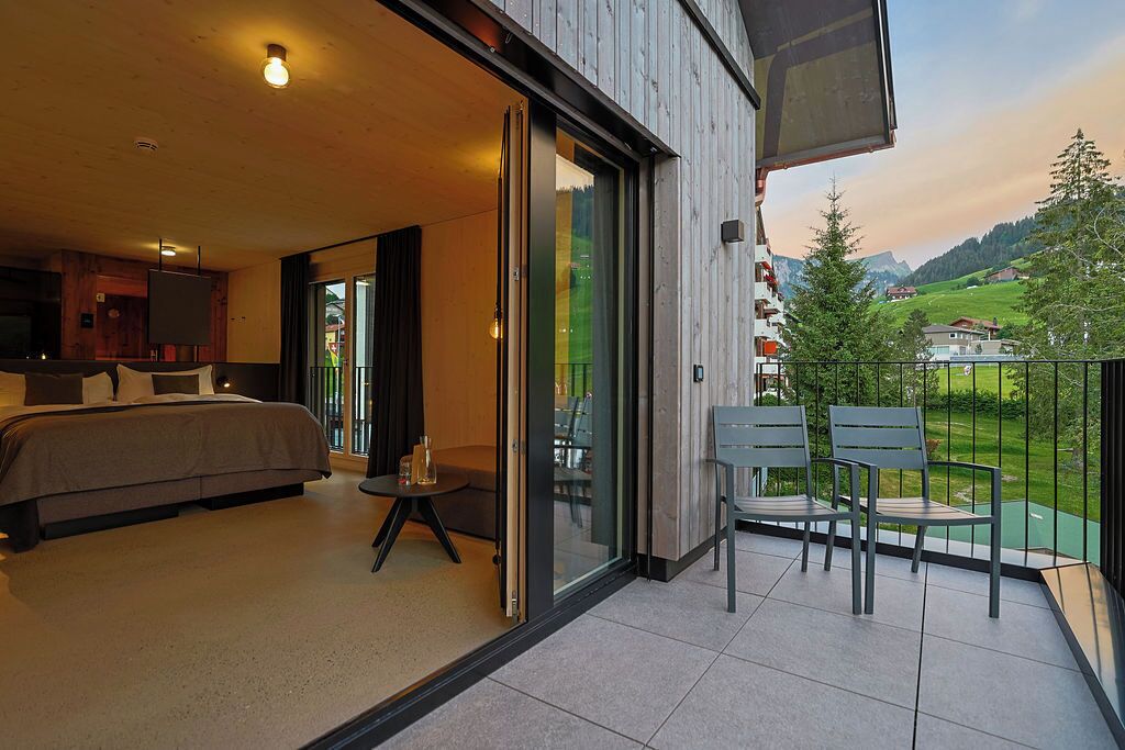 A modern bedroom with a bed, a small table, and a balcony with chairs.