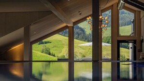 Ein geräumiger Raum mit großen Fenstern und Blick auf eine grüne Landschaft, einer modernen Kronleuchter und einem spiegelnden Boden.